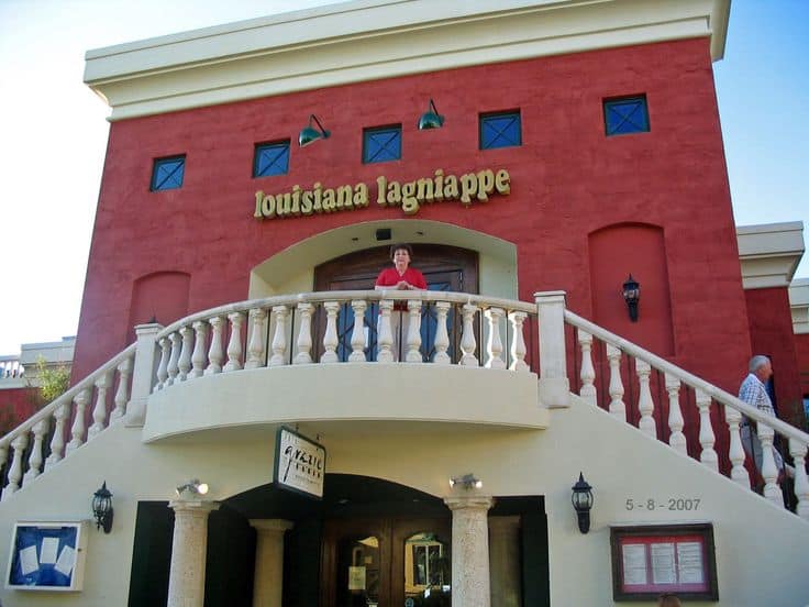 A person stands on a balcony in front of a red building with the sign